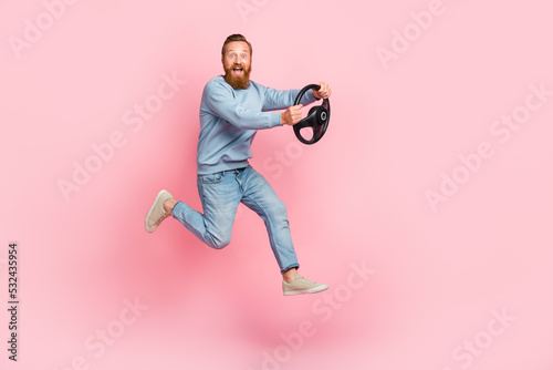 Full length profile portrait of energetic cheerful man jump arms hold wheel isolated on pink color background © deagreez
