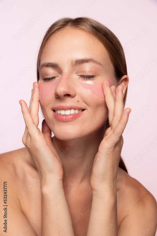 Half-legnth portrait of smiling beautiful girl with naked shoulders applying eye patches isolated over white background Half-legnth portrait of smiling beautiful girl with naked shoulders applying eye patches isolated over white background