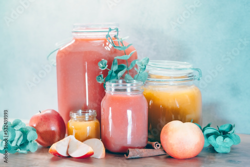 Apple and damson jam and other autumn season fruits in the glass jars. Red and yellow colored jam with apples, leaves and cinnamon around. 