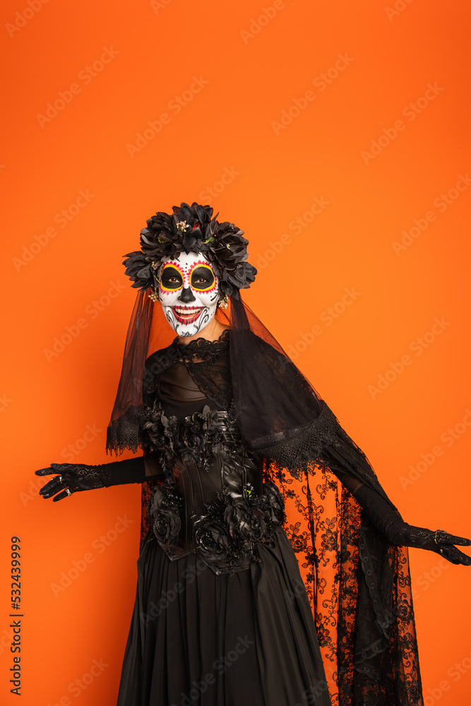 smiling woman in black witch dress and spooky halloween makeup isolated on orange.