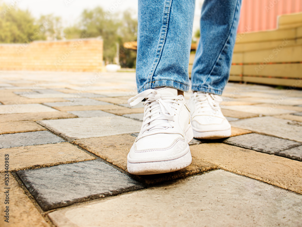 man or woman in white sneakers and in jeans on the sidewalk selective focus, men's shoes, women's shoes, walking in white sneakers man or woman in white sneakers and in jeans on the sidewalk selective focus, men's shoes, women's shoes, walking in white sneakers