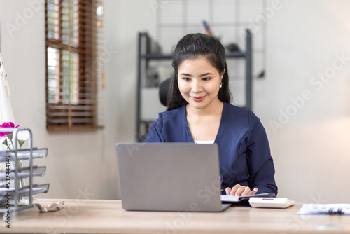 Young Asian female freelancer employee working with laptop at home and papers on desk workplace 