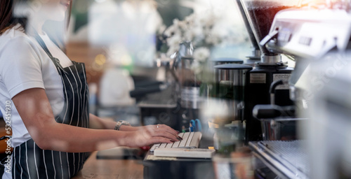 Young female asian Coffee Shop Owner is Working on Computer and Checking Inventory in a Cozy Cafe.