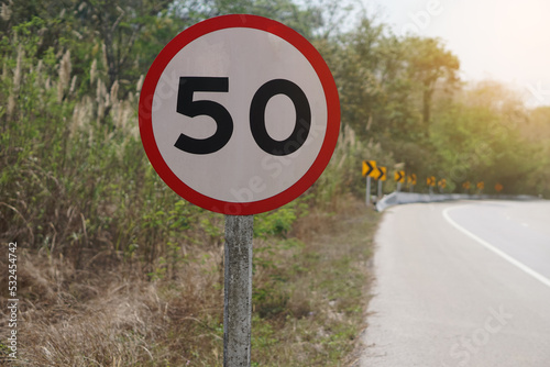 Circle road sign with number 50, installed beside the road in rural of Thailand. Speed limit for 50 km. per hour  for warning to slow driving on curve street. Traffic sign.                  