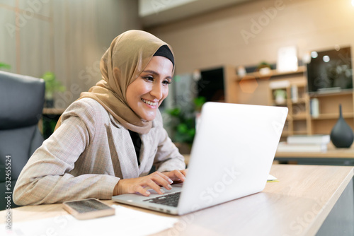 happy business muslim hijab woman work. the cheerful female islam worker looking at laptop talking to other professional employee. diversity company with beautiful female arab having online meeting