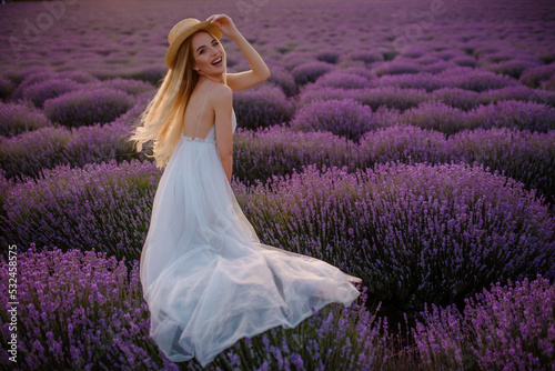 Young beautiful woman in a white dress and a hat is walking in the lavender field.