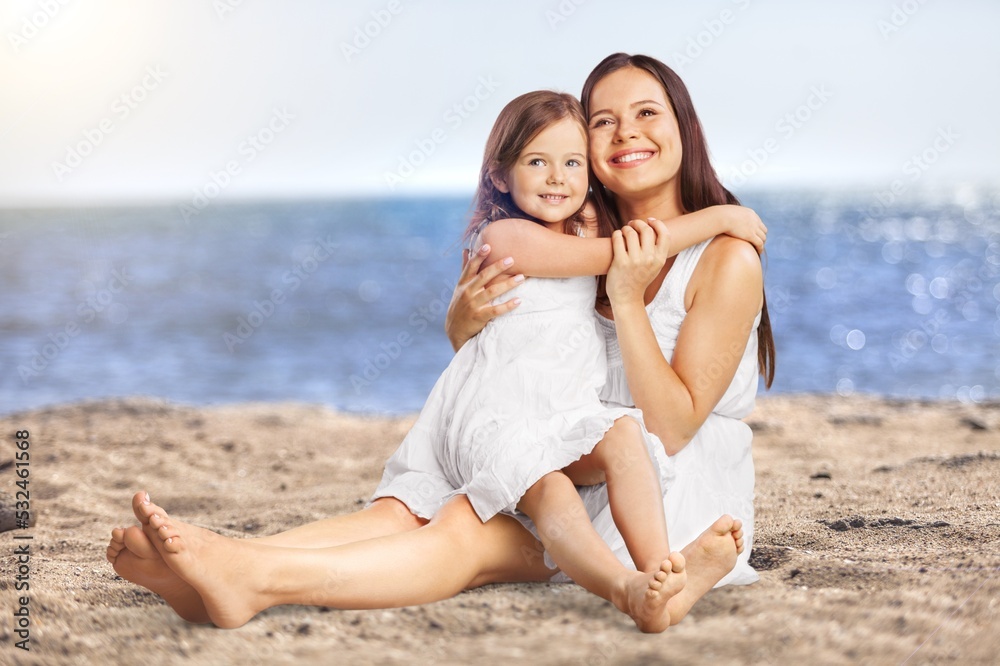Happy mother and daughter sitting on the beach.
