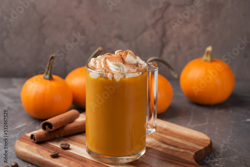 Autumn pumpkin spice latte with cream in mug on dark table. Traditional Coffee Drink for Autumn Holidays. A table decorated with mini pumpkins. Thanksgiving day or Halloween. Fall time.