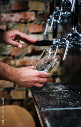 bartender hand at beer tap pouring a draught beer in glass serving in a bar or pub. tap room