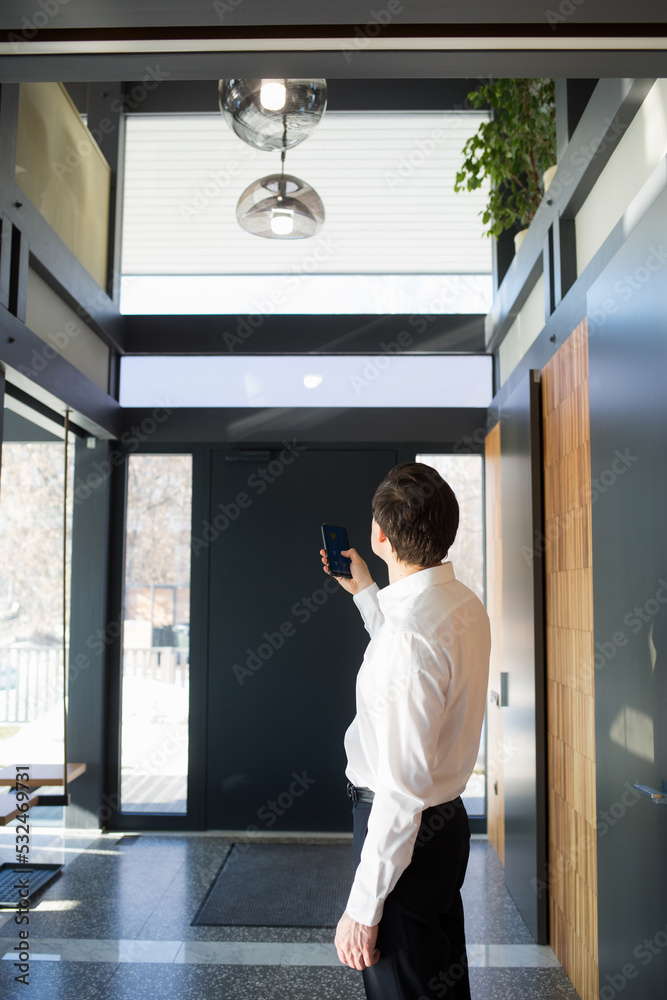 Fototapeta premium Man controlling home light with digital tablet in his house. Concept of smart home and light control with phone, mobile devices.
