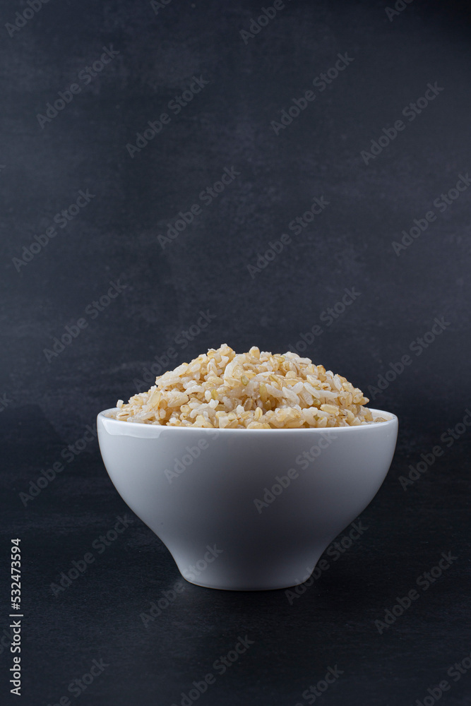 Brown rice in white rice bowl isolated on black background.