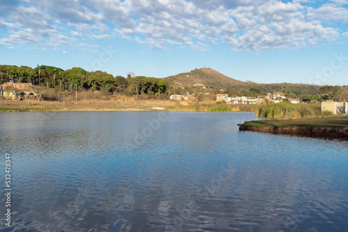 Nascer do sol entre nuvens, com céu azul e limpo, em frente a lagoa no bairro Jardim das Oliveiras, Esmeraldas, Minas Gerais, Brasil.