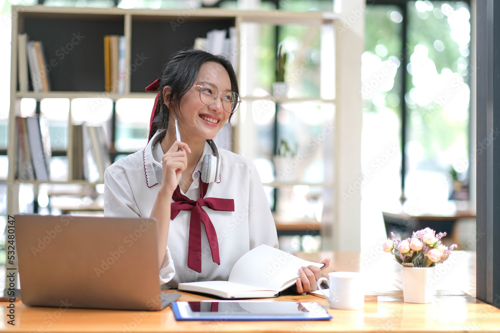 Happy young Asian student woman wearing headphones looking at webcam, looking at camera, during virtual meeting or video call talk.