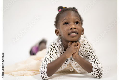 una bambina si sdraia a pancia in giù, e le braccia sotto il mento soridente con lo sfondo biancho  photo