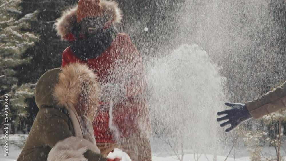 Slowmo of modern African American family with kid enjoying winter day in pine wood park playing with snow