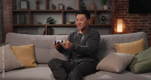 Happy Asian man using a wireless joystick and playing video games at home