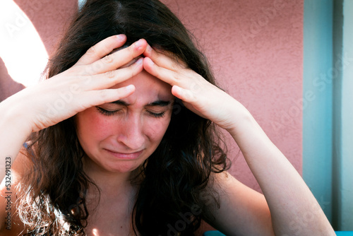 Photos A young caucasion girl is holding her forehead with her hands while crying