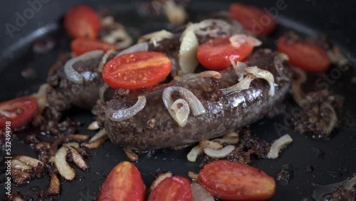 Hot black pudding with caramelized onion and tomatoes on pan, close-up. Blood pudding is a pork sausage filled with buckwheat and pork blood.