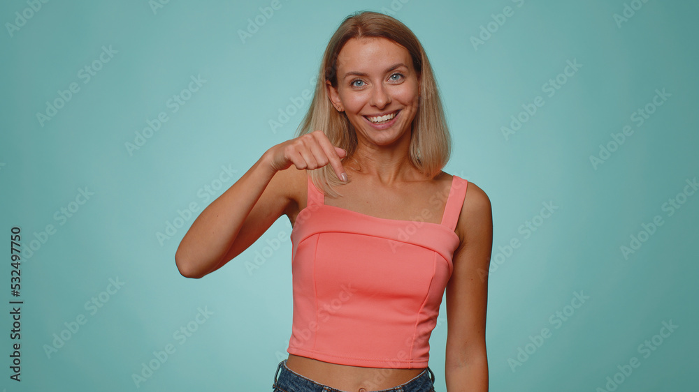 Subscribe. Woman pointing down, saying to look at advertisement, gesturing ok and like, showing place for commercial, promotional information below. Young girl isolated on blue studio wall background