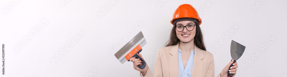 Girl engineer in an orange construction helmet with plastering painting tools in her hands on a white background. Girl engineer in an orange construction helmet with plastering painting tools in her hands on a white background.