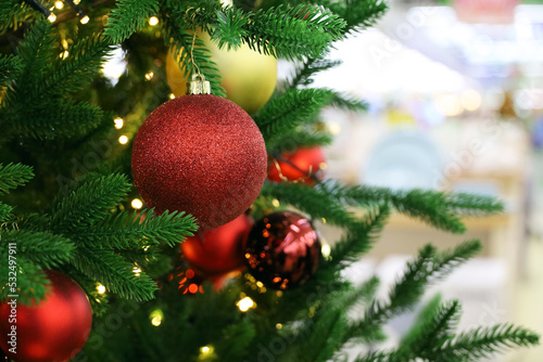 Christmas tree with red and golden toys in a shopping mall on background of blurred festive lights. New Year decorations  winter holidays and sale