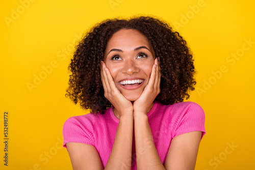 Photo of pretty positive girl arms touch cheekbones look up empty space isolated on yellow color background