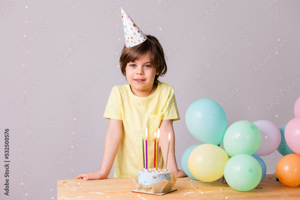 Cute little birthday boy in hat, cake with candles, balloons, happy birthday