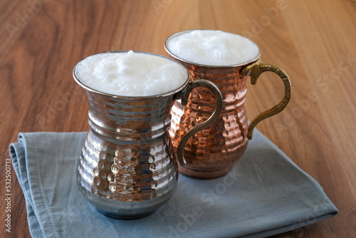 Buttermilk, Ayran - Traditional Turkish yoghurt drink with foam in a copper metal cup. Sparkling buttermilk in two copper glasses.