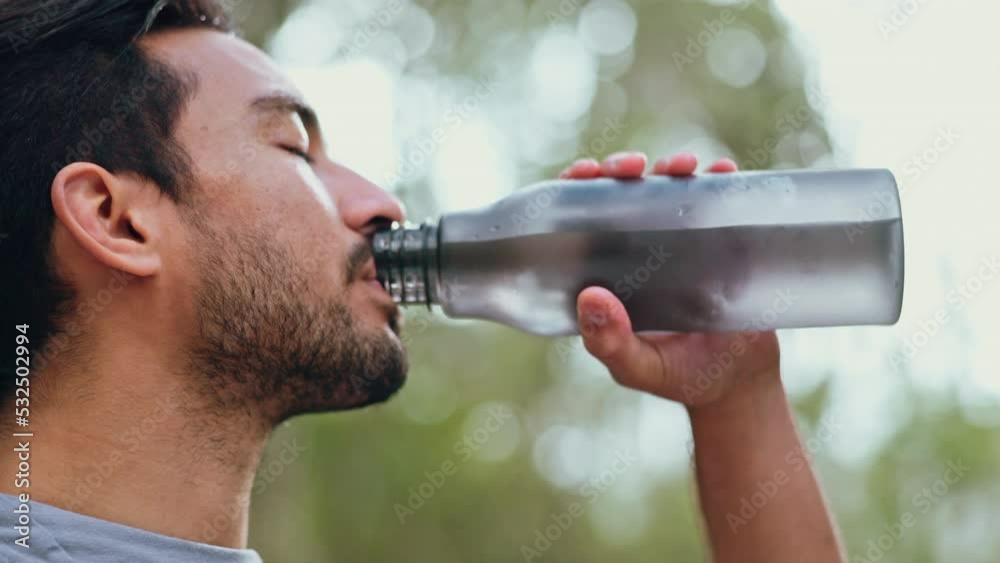 Man drinking water after workout and running outside, being healthy and hydrated. Portrait of male taking a sip of water from bottle after exercise in the park. Fitness, sports and training in nature
