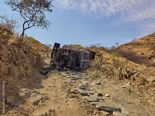 burnt out car wreck lying on its side on steep mountain pass photo