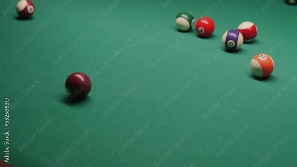 Multicolored billiard balls roll on the green table surface. Close up Multicolored billiard balls roll on the green table surface. Close up
