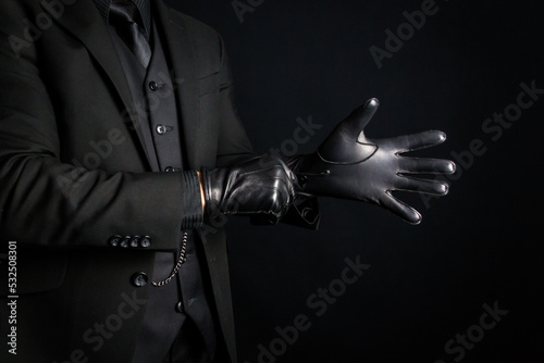 Portrait of Strong Man in Dark Suit Pulling on Black Leather Gloves. Concept of Mafia Hitman or Criminal Violence.