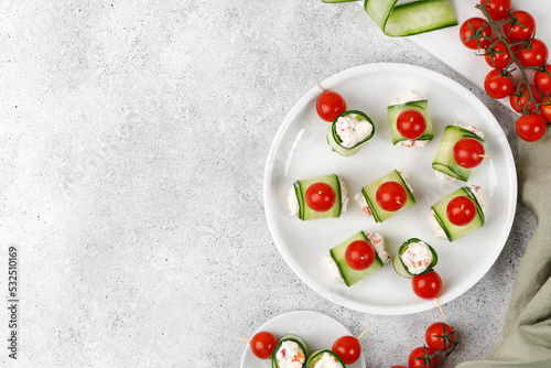 Cucumber rolls stuffed with cream cheese, tomatoes cherry over it, served on a white plate. Holiday vegetable appetizer, snack for a festive table. Mini fresh canapes.