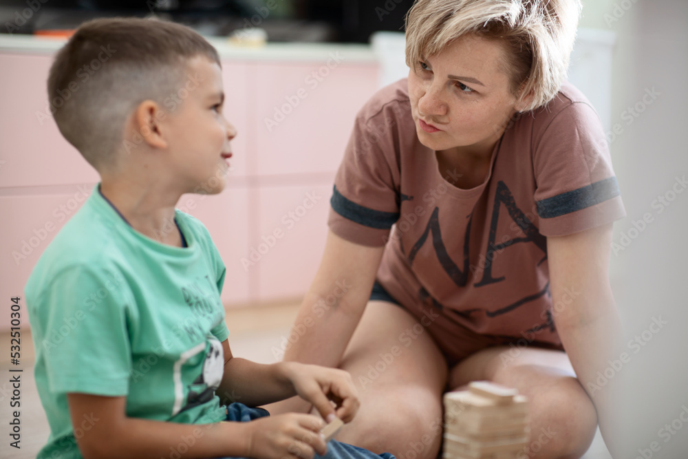 mom and son are playing a fun board game on laying wooden blocks in a tower and completing tasks while sitting on the floor at home having fun together mom and son are playing a fun board game on laying wooden blocks in a tower and completing tasks while sitting on the floor at home having fun together