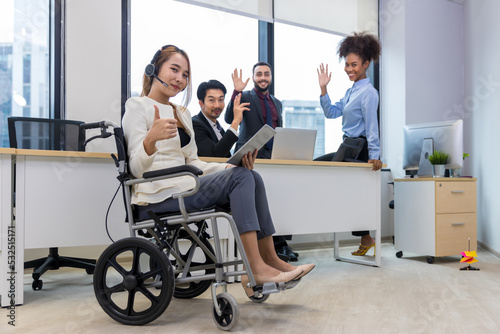 Office workers and woman on a wheelchair in bright office. They are showing a teamwork. Portrait of diverse business team with young woman in wheelchair all smiling at camera in office