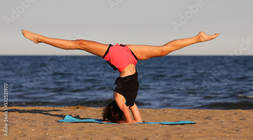 young slender athletic girl does exercises on gym mat on the beach