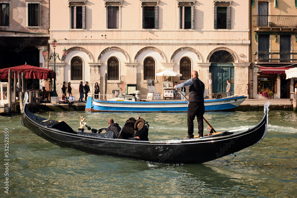 October 16, 2019, Venice, Italy: A gondola carrier takes a tourist along the Grand Canal, with a building and vacationers in the background October 16, 2019, Venice, Italy: A gondola carrier takes a tourist along the Grand Canal, with a building and vacationers in the background