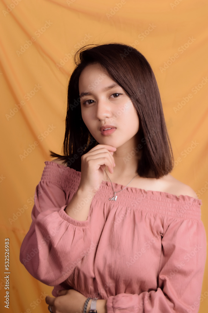 Young Asian woman wearing a pink crop top. Stand up and take half the body on a yellow background. Express emotions. Young Asian woman wearing a pink crop top. Stand up and take half the body on a yellow background. Express emotions.