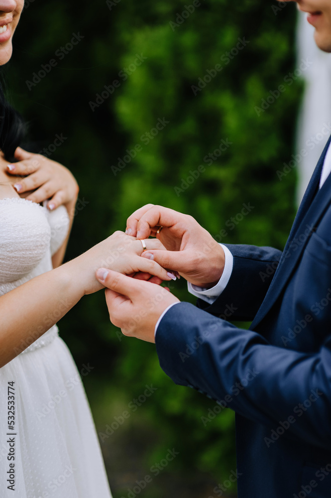 The groom in a blue suit puts a gold ring on the finger of the bride's hand at the ceremony. Wedding photography close-up of the newlyweds.