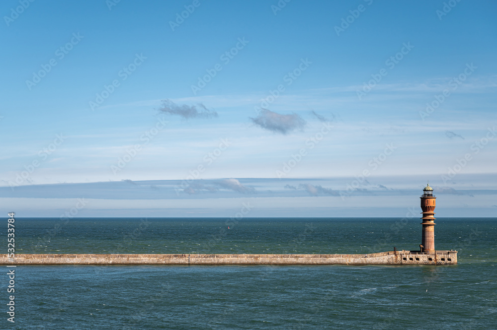 Europe, France, Dunkerque - July 9, 2022: Feu de Saint Pol, light tower, at end of its pier seen from inside harbor looking ove North Sea under blue cloudscape.