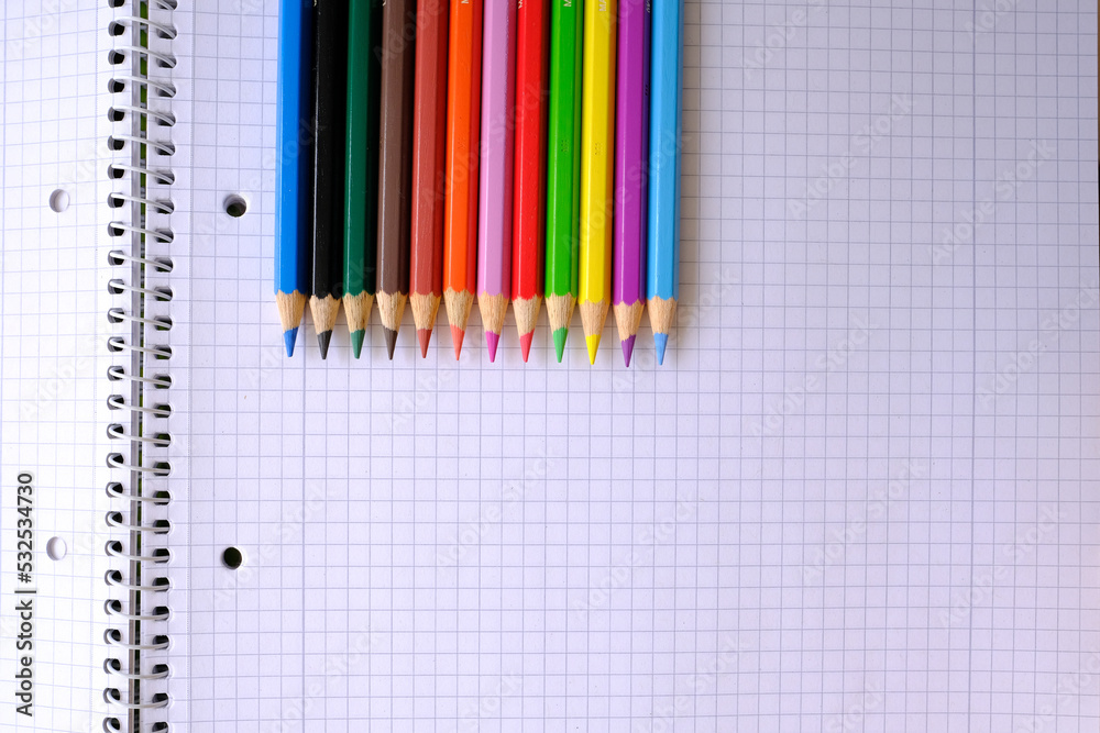 school background, colored pencils lie on a sheet of paper, an open notebook on a spiral, a college block in a cage, close-up, the concept of student writing supplies, back to school school background, colored pencils lie on a sheet of paper, an open notebook on a spiral, a college block in a cage, close-up, the concept of student writing supplies, back to school