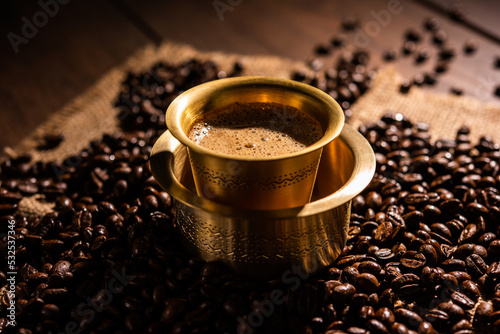 South Indian Filter coffee served in a traditional tumbler or cup over roasted raw beans photo