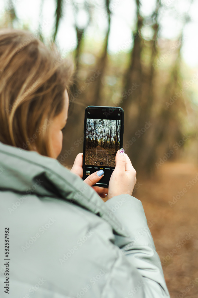 girl is holding a mobile phone and taking pictures in hand of nature, autumn landscape, digitalization of social networks