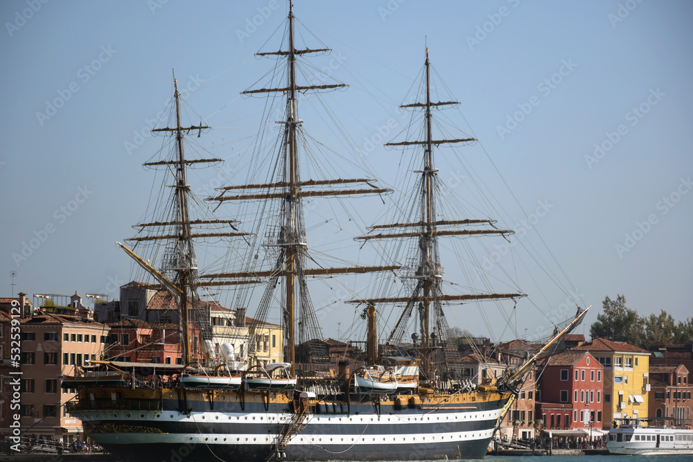 An ancient large ship stands near the pier in the port against the background of old low-rise buildings