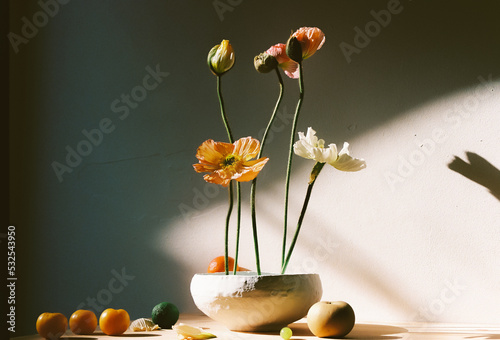 
various poppies and fruits placed in a white vase