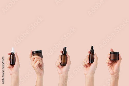 Beauty product and skin care remedy. Hand holding amber glass bottle which is cosmetic container on beige background.