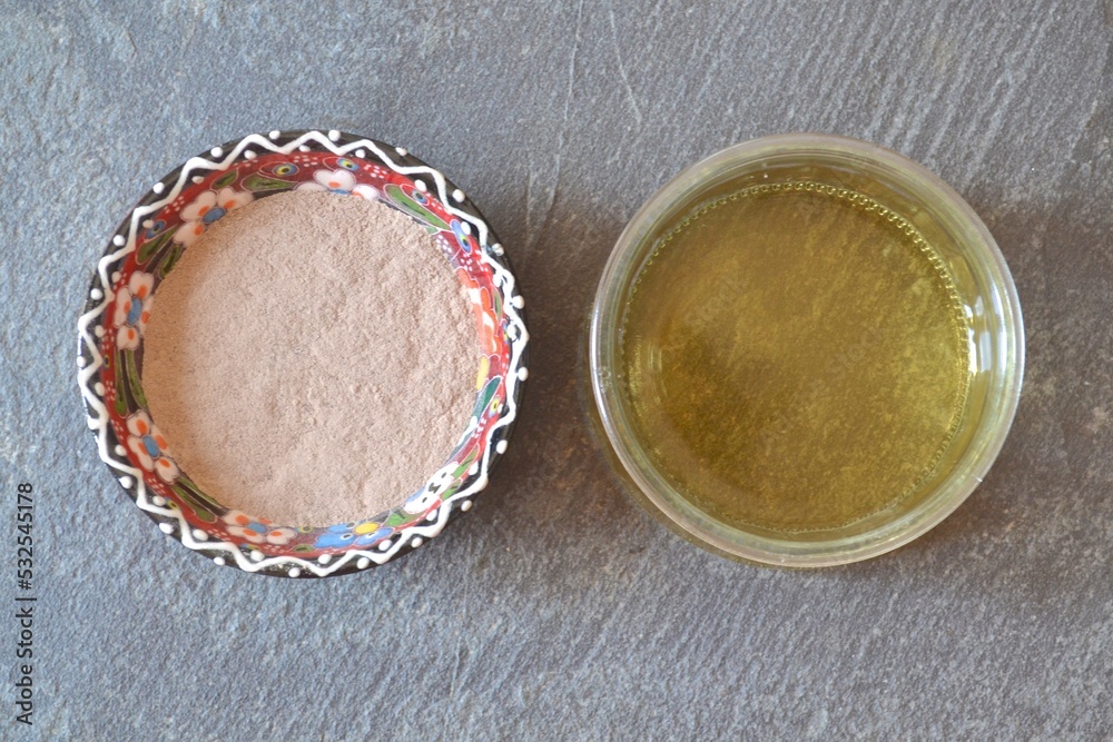 Top view of dry clay (rhassoul, ghassoul) in a colorful porcelain bowl with apple cider vinegar on a gray stone background. Top view of dry clay (rhassoul, ghassoul) in a colorful porcelain bowl with apple cider vinegar on a gray stone background.