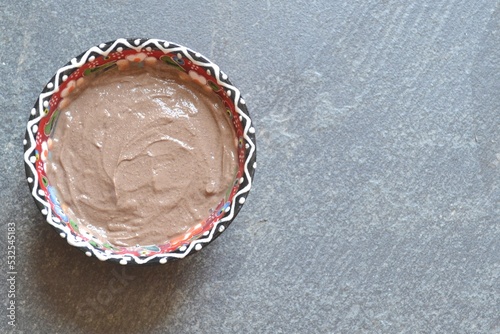 Top view of wet clay (rhassoul, ghassoul) in a colorful porcelain bowl on a gray stone background.