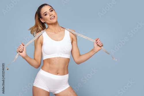 Cheerful slim woman measuring her body with tape .Fit young lady in perfect shape, happy with her shape. Weight Loss © neonshot
