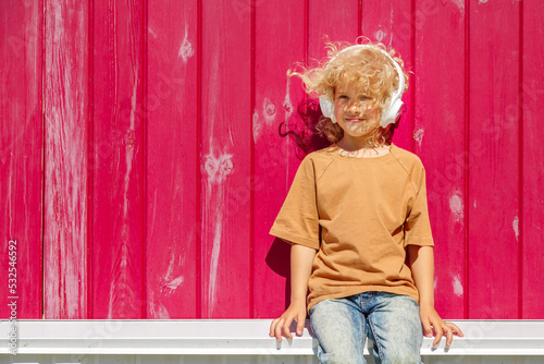 Blond girl with headphones resting outside house photo